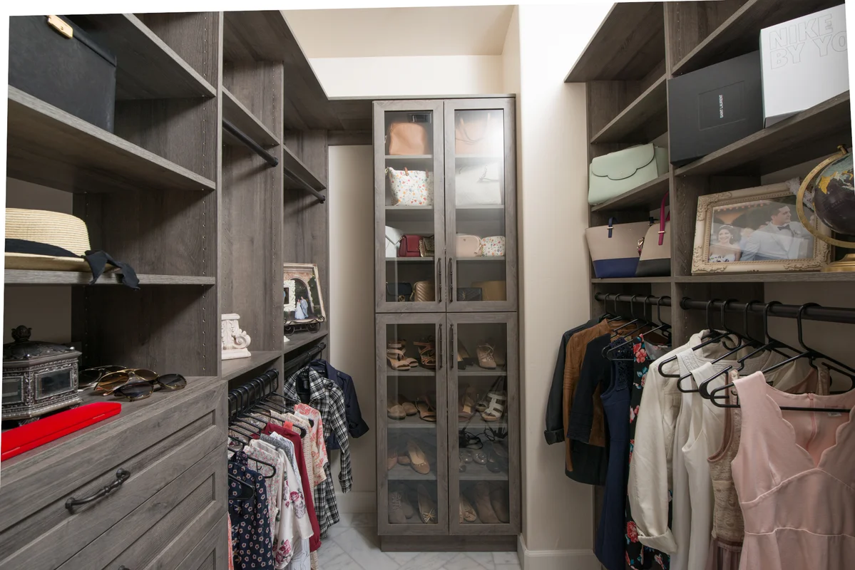Dark wood walk-in closet with glass cabinet doors